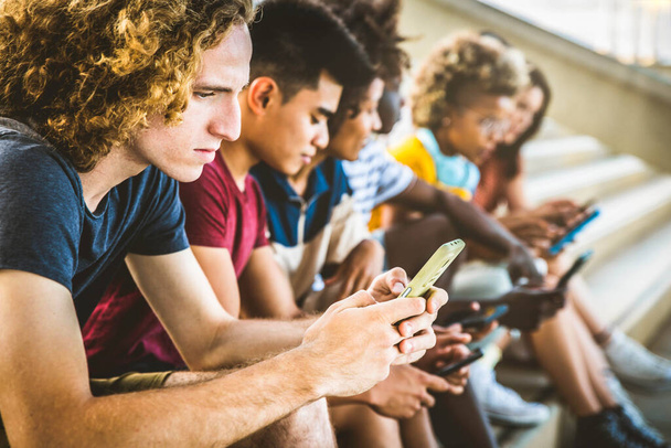大学のキャンパスに携帯電話を使って座っている大学生。流行技術と若者文化の概念 - 写真・画像