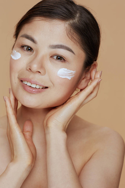 Portrait of modern woman with facial cream on face isolated on beige background. - 写真・画像