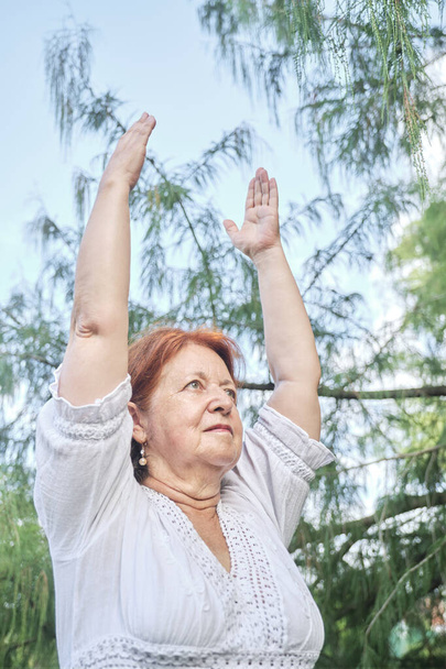 Mujer hispana mayor con ropa blanca que practica yoga al aire libre en un parque. Conceptos: bienestar, estilo de vida activo y saludable. - Foto, Imagen