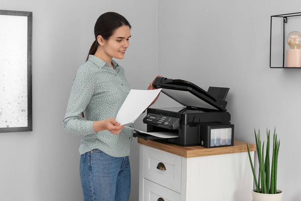Woman using modern printer on chest of drawers at home - Фото, изображение