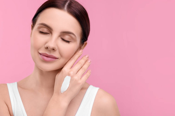 Beautiful woman with smear of body cream on her hand against pink background, space for text - Foto, immagini