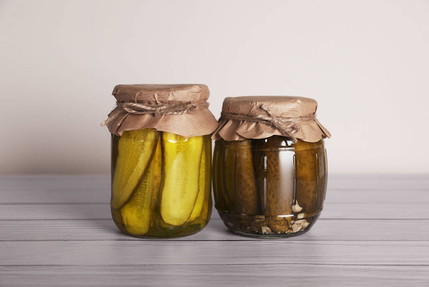 Jars with pickled cucumbers on white wooden table - Фото, изображение