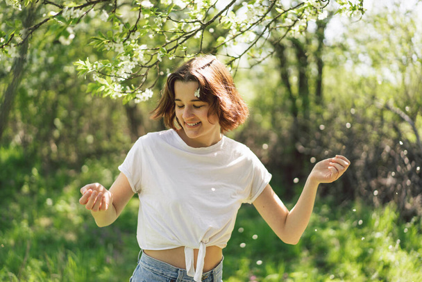 Krásná dospívající dívka s jarní květiny těší přírodu a směje se na jarní zahradě. Holka držící větev třešně. Koncept svobody a štěstí. Jaro. - Fotografie, Obrázek