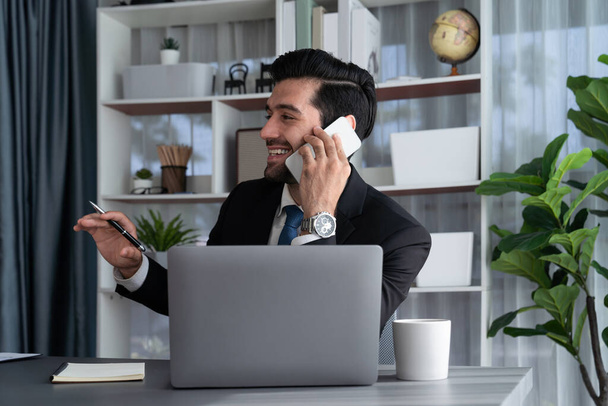 Homme d'affaires diligent occupé à parler sur l'appel téléphonique avec les clients tout en travaillant avec ordinateur portable dans son bureau comme concept de style de vie de travailleur de bureau moderne avec téléphone mobile. Fervent - Photo, image
