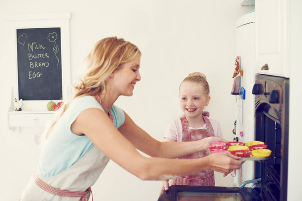 Στο φούρνο τώρα... χαριτωμένο κοριτσάκι ψήνει στην κουζίνα στο σπίτι με τη μαμά της - Φωτογραφία, εικόνα
