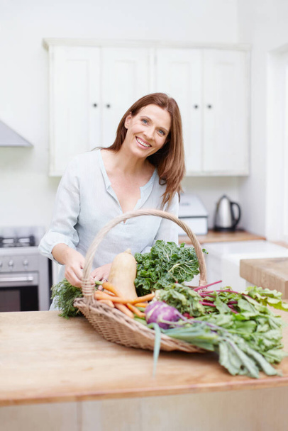 I picked this myself. A beautiful woman in her kitchen with a basket full of fresh vegetables - Foto, imagen