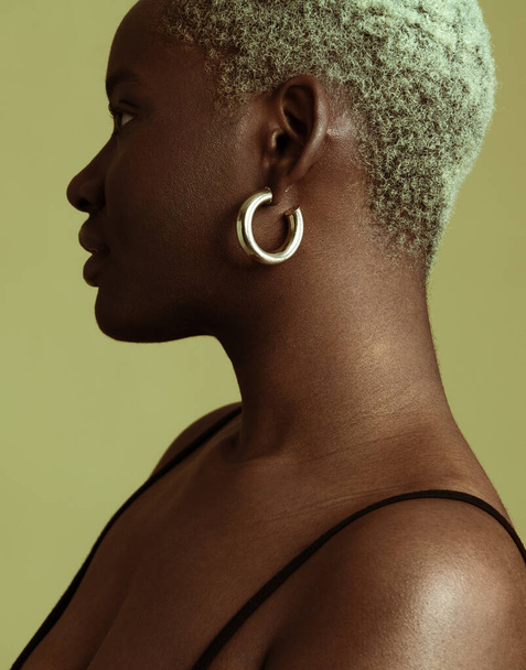 Side view of young African female with earrings and short Afro hair standing against green background looking away - Zdjęcie, obraz