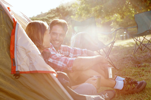 They enjoy their camping trips. A young couple talking at the entrance to their tent - Foto, imagen