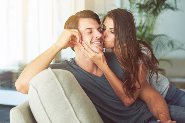 Woman, kiss and man on cheek for couple relax at home in love, intimacy and happy spending time together. Happiness, commitment or trust in relationship with people in living room, affection and care. - Foto, Imagem
