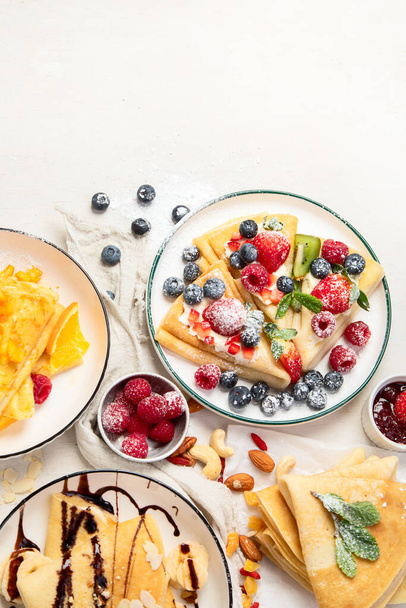 Variety of fresh crepes with chocolate, jam, fruits and berries on white background. Homemade delicious crepes. Top view. Copy space. - Foto, Bild