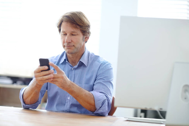Wireless technology in the workplace. a mature businessman reading a text message while sitting at his desk - Foto, Imagen