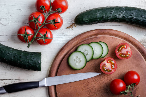 Pepino y tomates cortados con cuchillo de cocina en la mesa vieja blanca - Foto, Imagen