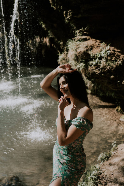 Beautiful model in a turquoise dress posing near a mountain waterfall.Wildlife concept - Photo, image