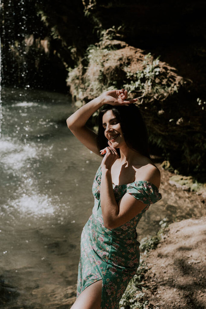Όμορφο μοντέλο με τιρκουάζ φόρεμα που ποζάρει κοντά σε καταρράκτη βουνού.Έννοια άγριας ζωής - Φωτογραφία, εικόνα