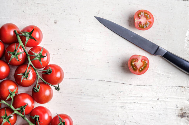 Banda czerwonych pomidorów wiśniowych pociętych nożem kuchennym na białym starym stole - Zdjęcie, obraz