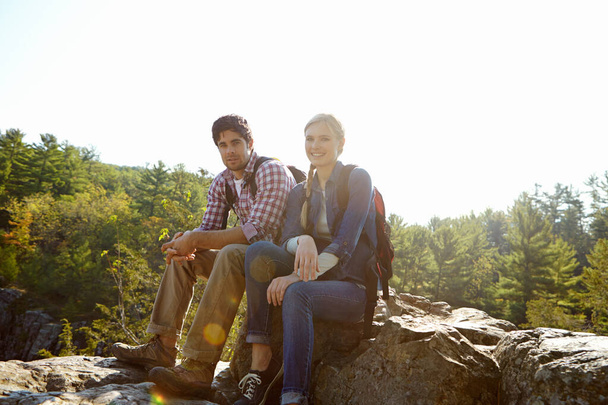 Taking a break from their hike. An attractive young couple sitting atop a moutain in a nature reserve - Foto, imagen