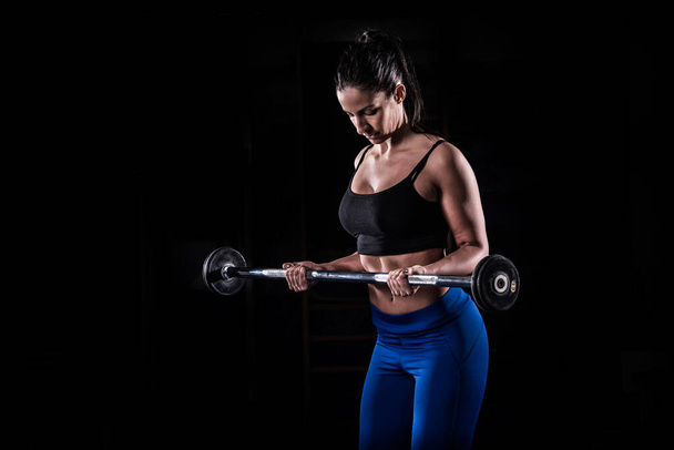 Bodybuilderin hebt Langhantel isoliert über schwarzem Hintergrund - Foto, Bild