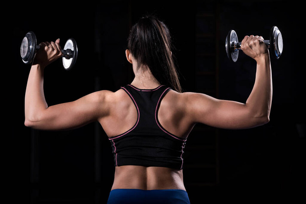 Woman bodybuilder lifting dumbbells isolated over black background - Photo, Image
