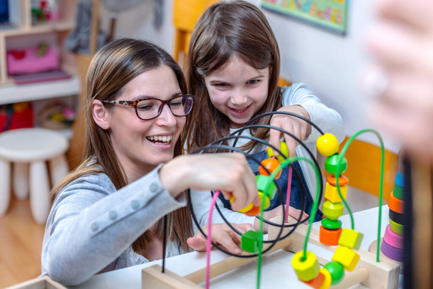 Kindergarten teacher looking at kid playing with didactic colorful toys indoors - preschool - Photo, Image