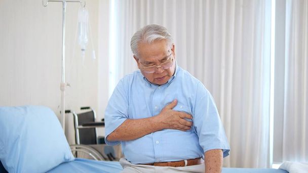 Elderly Asian man with chest pain suffering from heart attack. Man clutching his chest from acute pain. Heart attack symptom-Healthcare and medical concept - Foto, afbeelding