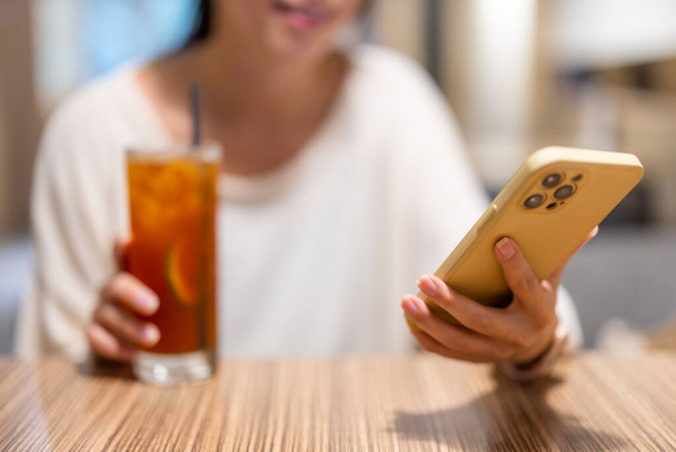 Kobieta pić mrożonej herbaty cytrynowej z telefonu komórkowego - Zdjęcie, obraz