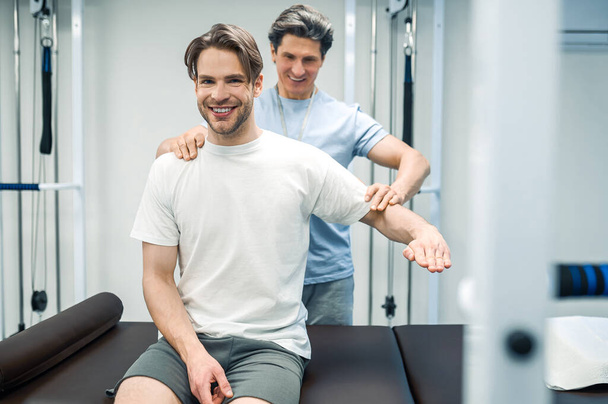 Recovery exercising. Male physical therapist working with a patient and looking invloved - Zdjęcie, obraz