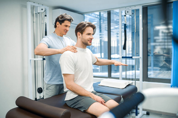 Recovery exercising. Male physical therapist working with a patient and looking invloved - Photo, image