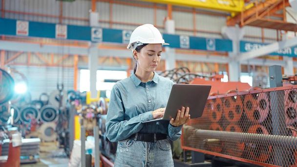 Руководитель-инженер женщина в шлеме держит ноутбук стоя и проверить на рабочем месте на заводе. Концепция заводов и промышленных предприятий - Фото, изображение