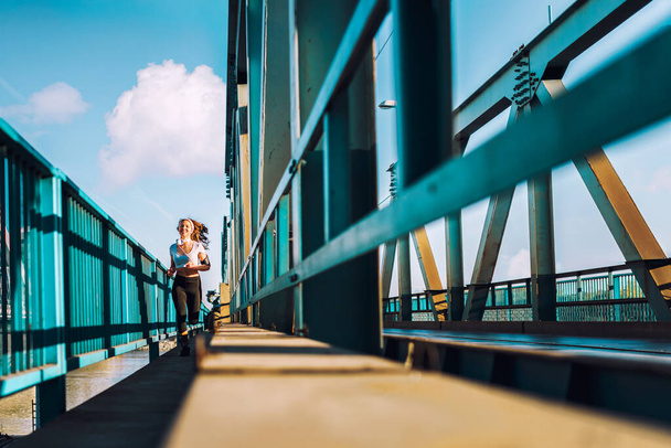νεαρή γυναίκα δρομέας σε κολάν τρέχει στη γέφυρα της πόλης - Φωτογραφία, εικόνα