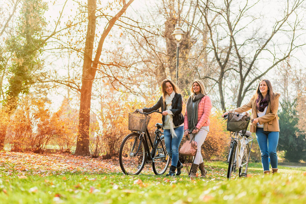 Grupa uśmiechniętych studentek z rowerami spacerujących po parku - przyjaźń - Zdjęcie, obraz