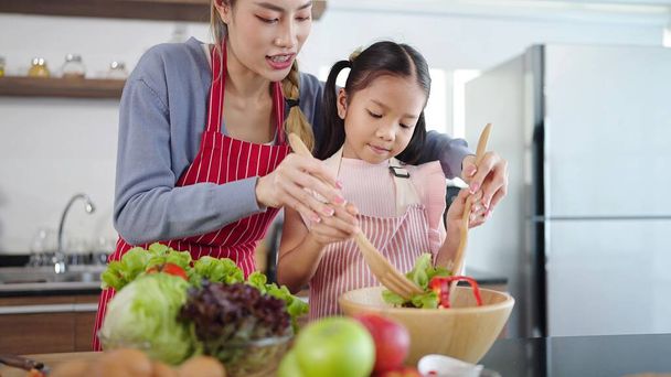 Asian mother and daughter cooking together in kitchen are preparing healthy food. Happy Asian family making salad enjoy family activity together - Foto, imagen