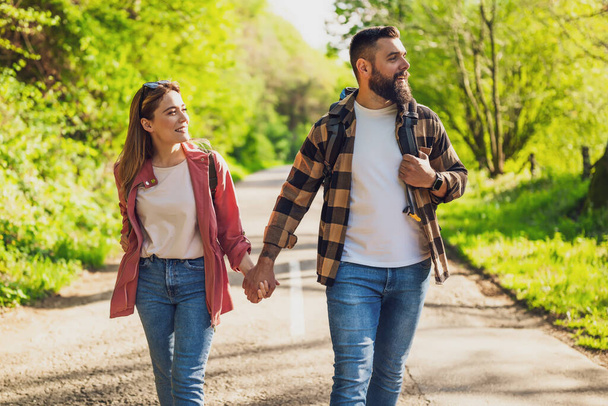 Happy couple hiking in nature on sunny day. Couple holding hands and walking on road. - Photo, Image