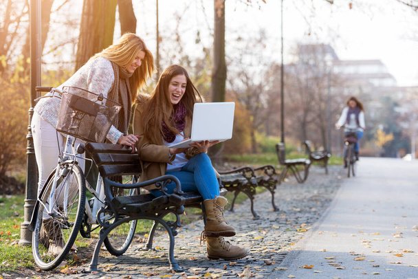 Group of smiling college girls on park bench working on laptop - Zdjęcie, obraz