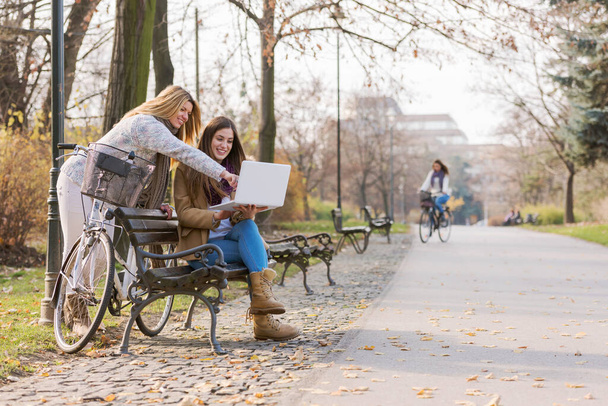 Group of smiling college girls on park bench working on laptop - Photo, Image