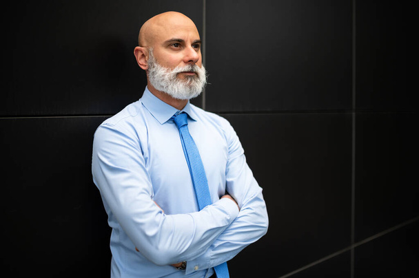 Mature bald stylish businessman portrait with a white beard outdoor with folded arms - Photo, image