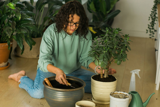 Smiling young woman and pot with plant happy work in indoor garden or cozy home office with different houseplants. Happy millennial female gardener florist take care of domestic flower - Valokuva, kuva