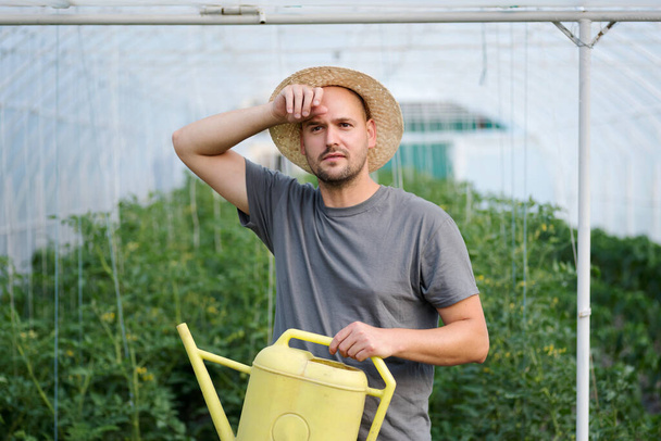 Young tired farmer wiping off his sweat after working in a greenhouse - Foto, Imagen