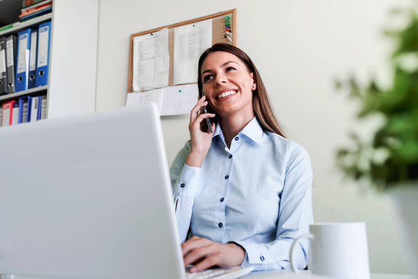 Podnikatelka v kanceláři pracuje na notebooku mluvit po telefonu - Fotografie, Obrázek