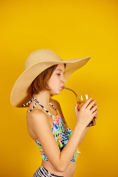 Παιδί έφηβος κορίτσι με μαγιό και ψάθινο καπέλο με λεμονάδα μεταλλικό καλαμάκι στο στούντιο σε κίτρινο φόντο, καλοκαιρινή διάθεση, - Φωτογραφία, εικόνα