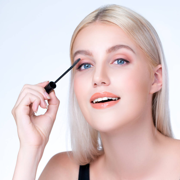 Closeup personable woman with blond hair putting black mascara with brush in hand on long thick eyelash. Perfect fashionable cosmetic clean facial skin with beautiful eye young woman. - Fotó, kép