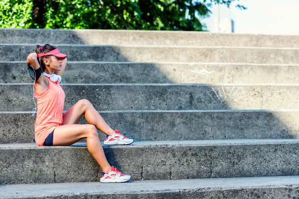 Sporty jogging girl sitting outdoors resting after training - Photo, image