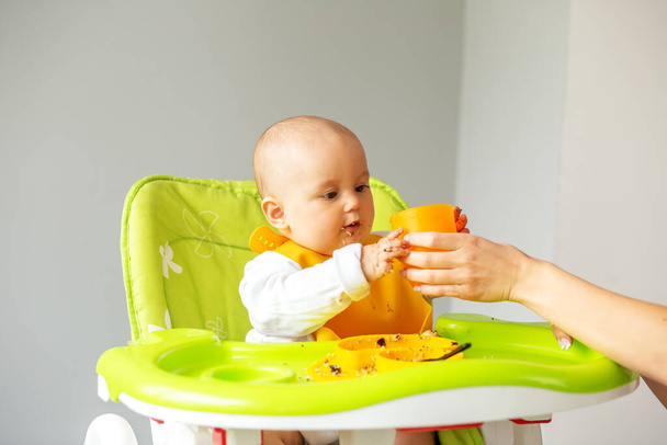 A bébiszitter a konyhában eteti a kisbabát. Etetőasztal. Szék beállítva. Hordozható baba. Baba erősítő. Hordozható összecsukható - Fotó, kép