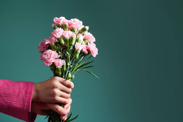 As mãos de uma menina segurando um buquê de cravos rosa em um fundo azul-turquesa verde. Parabéns. Obrigado. Conceito para o Dia das Mães. Espaço de cópia. - Foto, Imagem