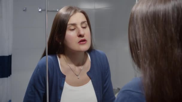 Egy fiatal nő áll a mosdókagylónál és tükörbe néz. A depresszió, a stressz, a mentális betegségek és problémák, a magány és a frusztráció fogalma - Felvétel, videó