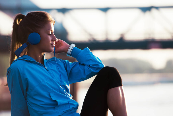 Young woman jogger resting listening music by the river - Foto, imagen