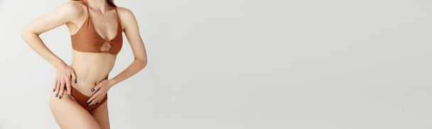 Procedimientos de protección solar. Imagen recortada de cuerpo femenino delgado con piel clara en traje de baño con protector solar en el vientre sobre fondo blanco del estudio. Banner. Concepto de salud, spf, vacaciones, verano, anuncio - Foto, imagen