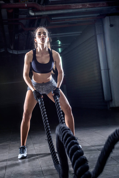 Battle ropes session. Attractive young fit and toned sportswoman working out in fitness training gym - Фото, зображення