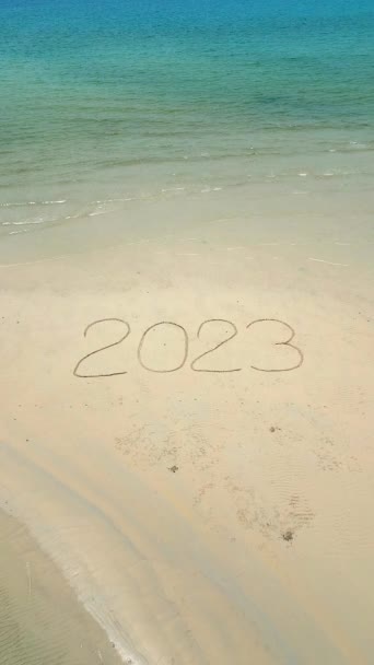 Luchtfoto van het woord 2023 geschreven op het witte zand op een tropisch strand omgeven door turquoise oceaan water. - Video
