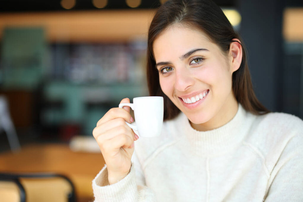 Happy woman smiling holding coffee cup in a bar looking at camera - Fotografie, Obrázek