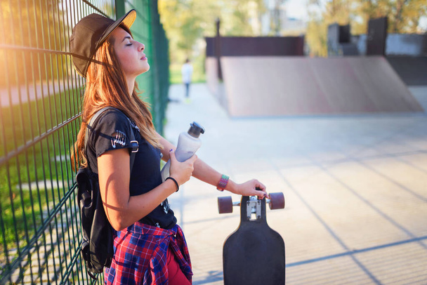 Roztomilý městský dívka držení longboard v skate parku s lahví vody - Fotografie, Obrázek